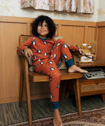 Child wearing the Maxomorra kids dragons organic cotton long sleeve top with pyjama trousers. Red top with repeat blue dragon print and blue arm cuffs and binding on the neck. 
