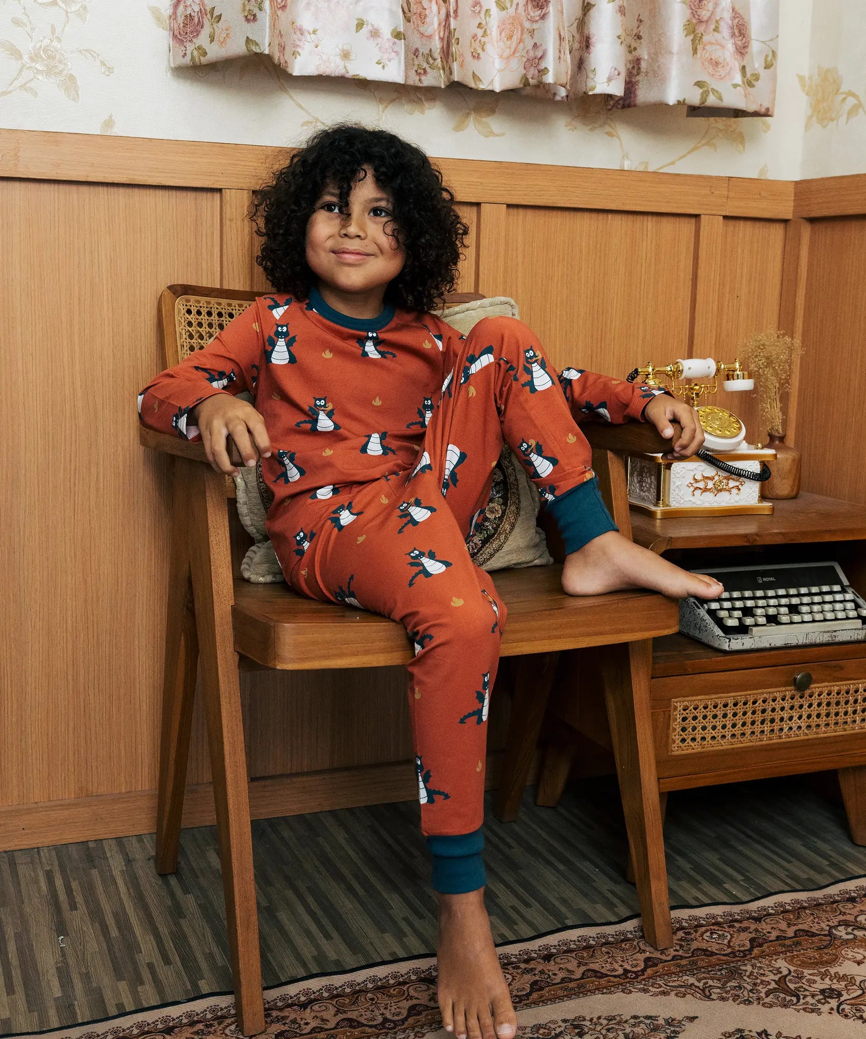 Child wearing the Maxomorra kids dragons organic cotton long sleeve top with pyjama trousers. Red top with repeat blue dragon print and blue arm cuffs and binding on the neck. 
