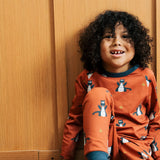 Child wearing the Maxomorra kids dragons organic cotton long sleeve top with pyjama trousers. Red top with repeat blue dragon print and blue arm cuffs and binding on the neck. 
