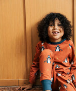 Child wearing the Maxomorra kids dragons organic cotton long sleeve top with pyjama trousers. Red top with repeat blue dragon print and blue arm cuffs and binding on the neck. 
