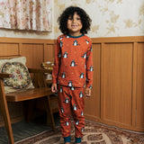 Child wearing the Maxomorra kids dragons organic cotton long sleeve top with pyjama trousers. Red top with repeat blue dragon print and blue arm cuffs and binding on the neck. 
