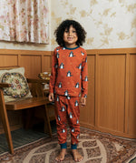 Child wearing the Maxomorra kids dragons organic cotton long sleeve top with pyjama trousers. Red top with repeat blue dragon print and blue arm cuffs and binding on the neck. 
