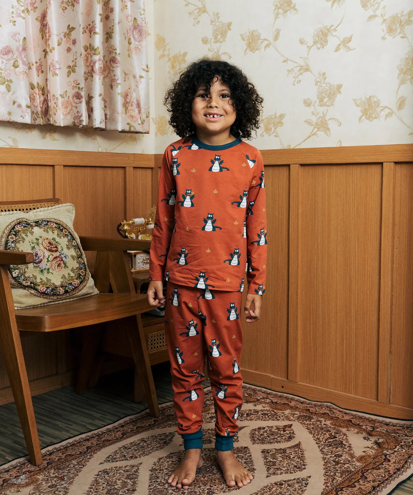 Child wearing the Maxomorra kids dragons organic cotton long sleeve top with pyjama trousers. Red top with repeat blue dragon print and blue arm cuffs and binding on the neck. 
