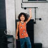 Child wearing the Maxomorra kids dragons organic cotton sleeveless vest with teal joggers. Rust red sleeveless vest top with repeat print featuring a blue dragon and yellow fire outlines with blue binding on the neck and arm holes. 
