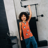 Child wearing the Maxomorra kids dragons organic cotton sleeveless vest with teal joggers. Rust red sleeveless vest top with repeat print featuring a blue dragon and yellow fire outlines with blue binding on the neck and arm holes. 
