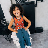 Child wearing the Maxomorra kids dragons organic cotton sleeveless vest with blue teal joggers. Rust red sleeveless vest top with repeat print featuring a blue dragon and yellow fire outlines with blue binding on the neck and arm holes. 
