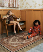 Two Children wearing Maxomorra organic cotton clothing. One is wearing a brown apple print vest and shorts the other is wearing a rust red blue dragon print long sleeved top with matching trousers.