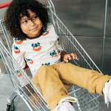 Child wearing the Maxomorra kids vikings organic cotton long sleeve top with mustard yellow trousers. Light coloured top with  repeat viking print and contrasting brown arm cuffs and binding on the neck. 
