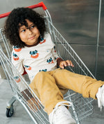 Child wearing the Maxomorra kids vikings organic cotton long sleeve top with mustard yellow trousers. Light coloured top with  repeat viking print and contrasting brown arm cuffs and binding on the neck. 
