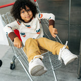 Child wearing the Maxomorra kids vikings organic cotton long sleeve top with mustard yellow trousers. Light coloured top with  repeat viking print and contrasting brown arm cuffs and binding on the neck. 
