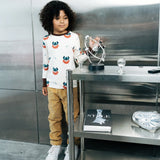 Child wearing the Maxomorra kids vikings organic cotton long sleeve top with mustard yellow trousers. Light coloured top with  repeat viking print and contrasting brown arm cuffs and binding on the neck. 
