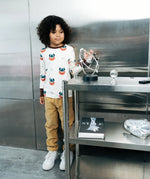 Child wearing the Maxomorra kids vikings organic cotton long sleeve top with mustard yellow trousers. Light coloured top with  repeat viking print and contrasting brown arm cuffs and binding on the neck. 
