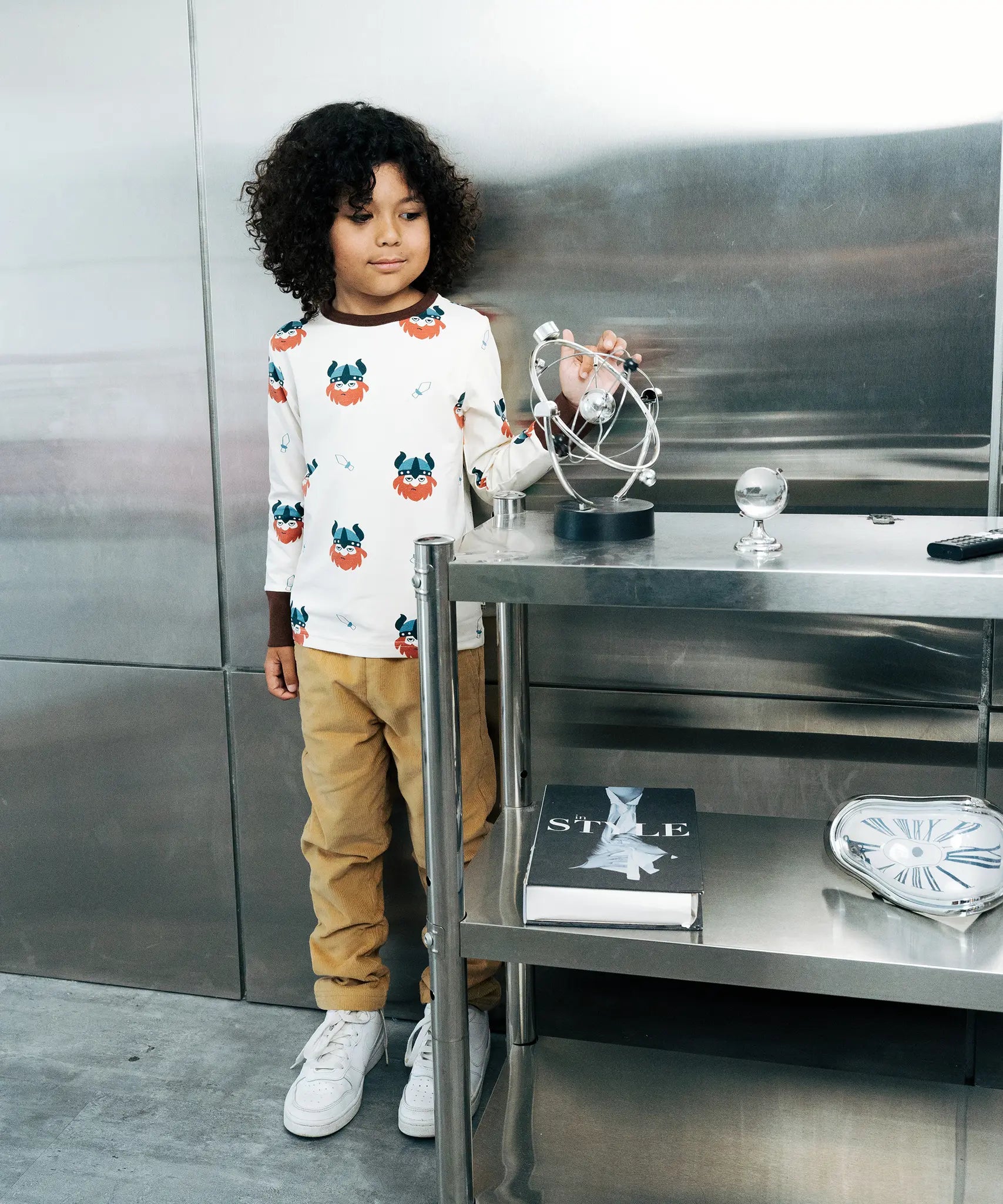 Child wearing the Maxomorra kids vikings organic cotton long sleeve top with mustard yellow trousers. Light coloured top with  repeat viking print and contrasting brown arm cuffs and binding on the neck. 
