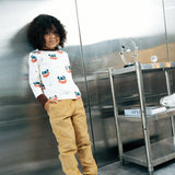 Child wearing the Maxomorra kids vikings organic cotton long sleeve top with mustard yellow trousers. Light coloured top with  repeat viking print and contrasting brown arm cuffs and binding on the neck. 
