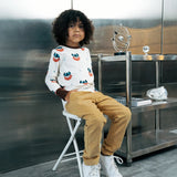 Child wearing the Maxomorra kids vikings organic cotton long sleeve top with mustard yellow trousers. Light coloured top with  repeat viking print and contrasting brown arm cuffs and binding on the neck. 
