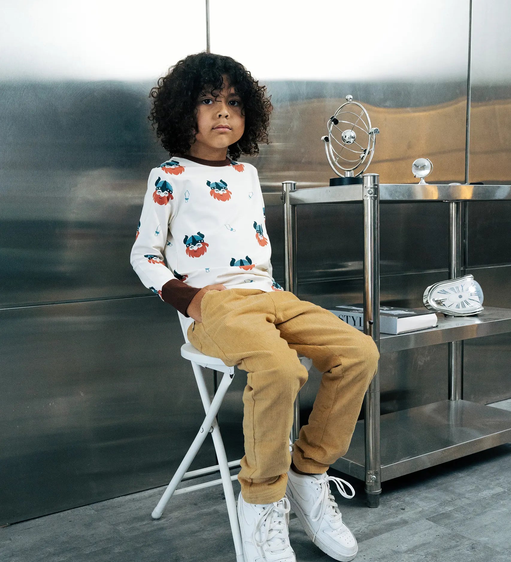 Child wearing the Maxomorra kids vikings organic cotton long sleeve top with mustard yellow trousers. Light coloured top with  repeat viking print and contrasting brown arm cuffs and binding on the neck. 
