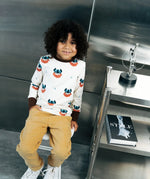 Child wearing the Maxomorra kids vikings organic cotton long sleeve top with mustard yellow trousers. Light coloured top with  repeat viking print and contrasting brown arm cuffs and binding on the neck. 
