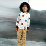 Child wearing the Maxomorra kids vikings organic cotton long sleeve top with mustard yellow trousers. Light coloured top with  repeat viking print and contrasting brown arm cuffs and binding on the neck. 
