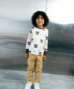 Child wearing the Maxomorra kids vikings organic cotton long sleeve top with mustard yellow trousers. Light coloured top with  repeat viking print and contrasting brown arm cuffs and binding on the neck. 
