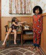 Two Children wearing Maxomorra organic cotton clothing. One is wearing a brown apple print vest and shorts the other is wearing a rust red blue dragon print long sleeved top with matching trousers.