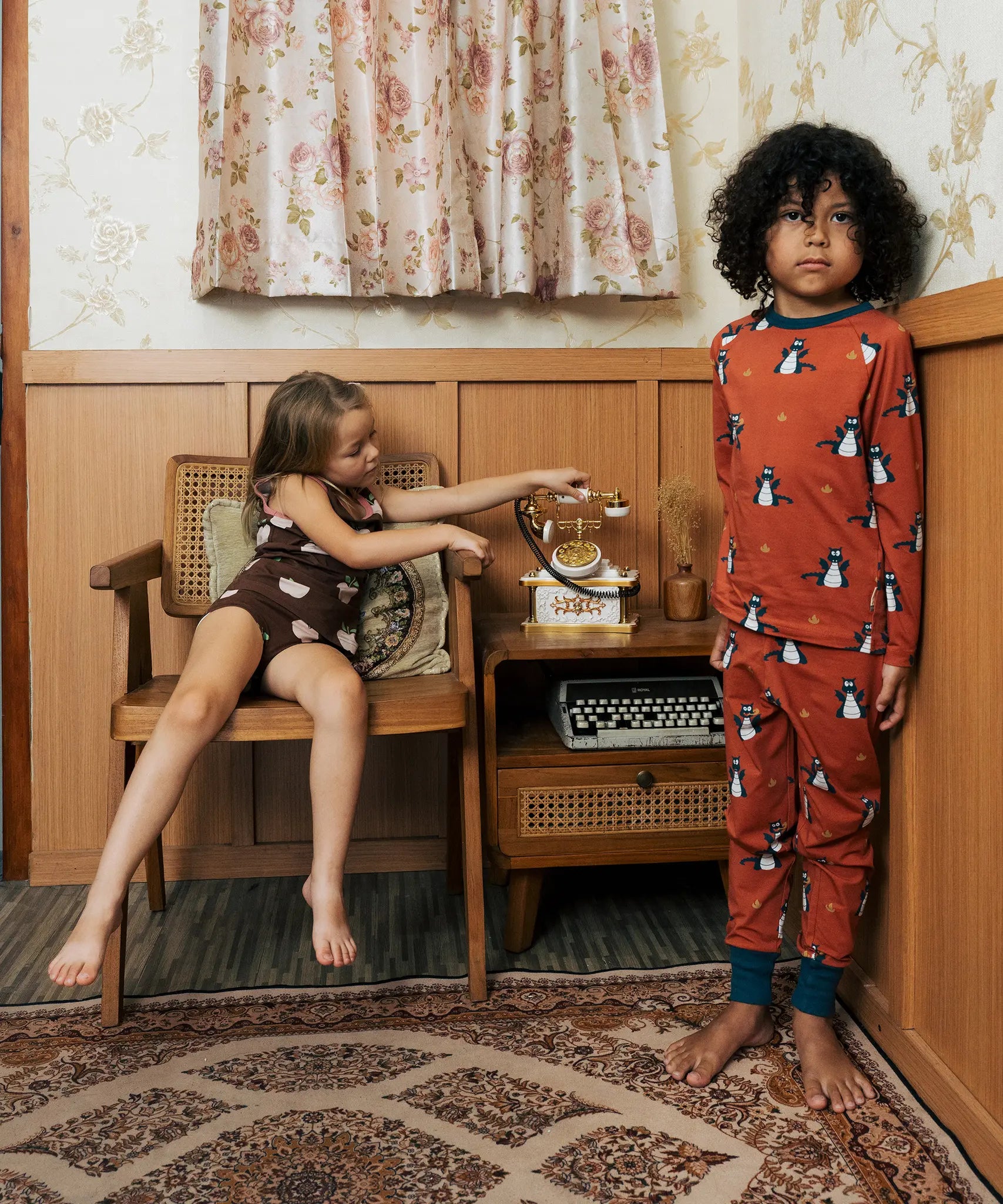 Two Children wearing Maxomorra organic cotton clothing. One is wearing a brown apple print vest and shorts the other is wearing a rust red blue dragon print long sleeved top with matching trousers.