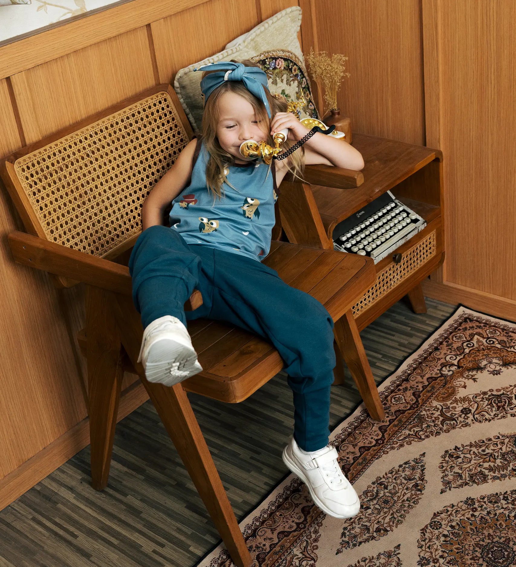 Child wearing the Maxomorra GOTS organic cotton kids tank vest top in blue with a cute repeating owl print and brown trim.with blue trousers.