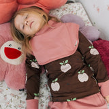 Child wearing the Maxomorra GOTS organic cotton long sleeve top in brown with a cute repeating pink apple print and pale pink neck line and cuffs with a pink snood bib scarf.