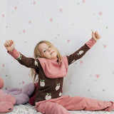 Child wearing the Maxomorra GOTS organic cotton long sleeve top in brown with a cute repeating pink apple print and pale pink neck line and cuffs with pink trousers.