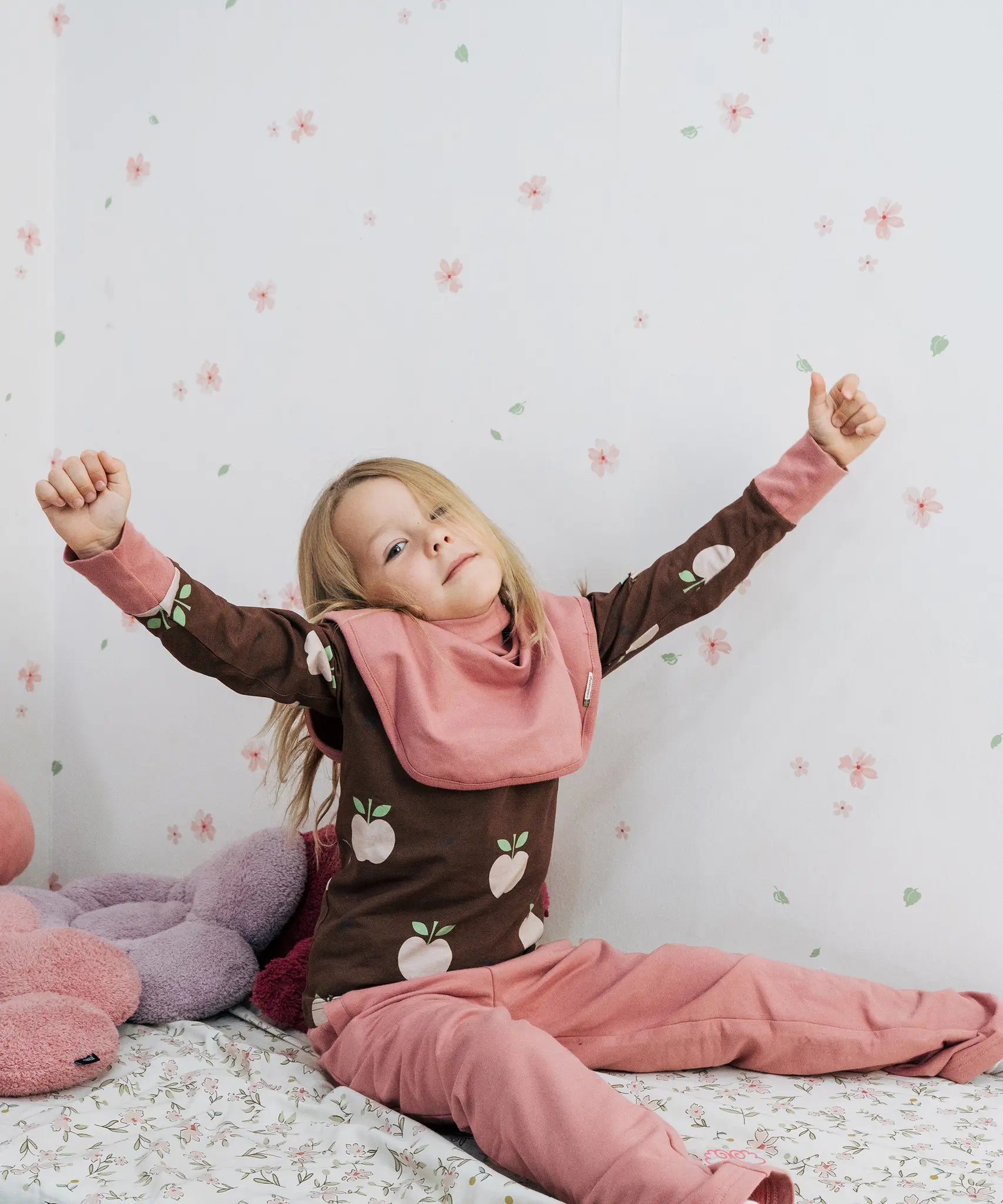 Child wearing the Maxomorra GOTS organic cotton long sleeve top in brown with a cute repeating pink apple print and pale pink neck line and cuffs with pink trousers.
