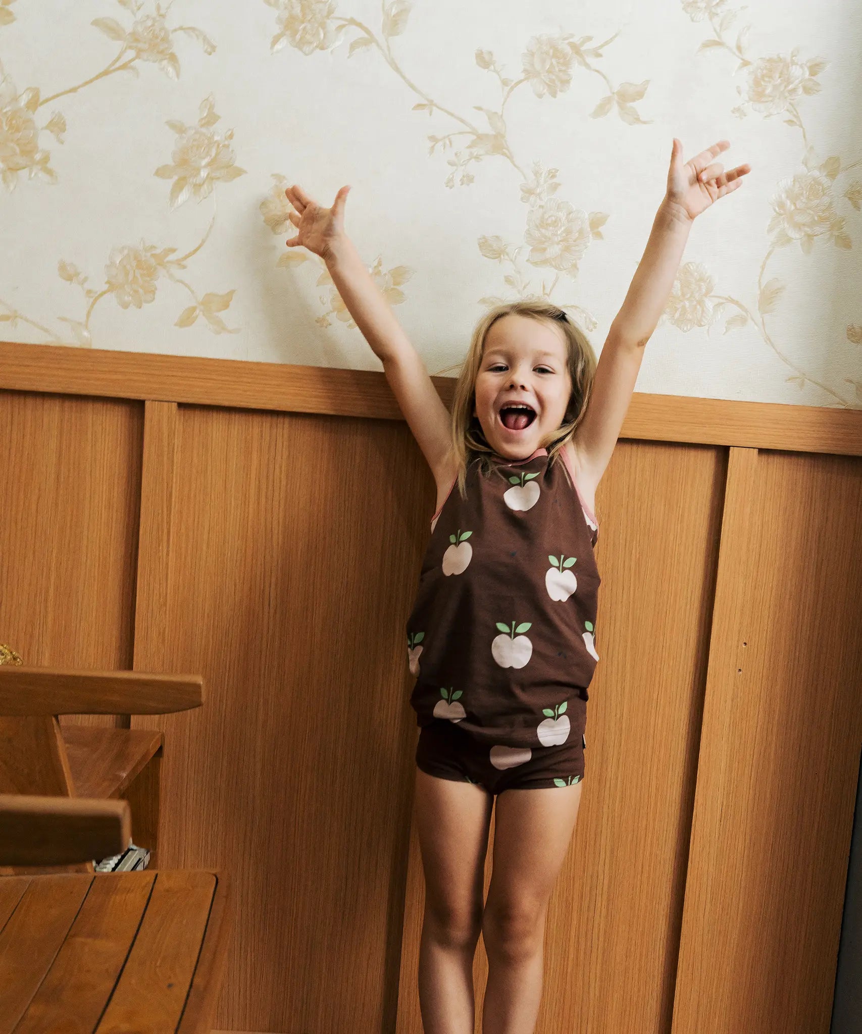 Girl wearing the Maxomorra's  GOTS organic cotton kids tank top in brown with a cute repeating pink apple print with matching trim with matching printpants.