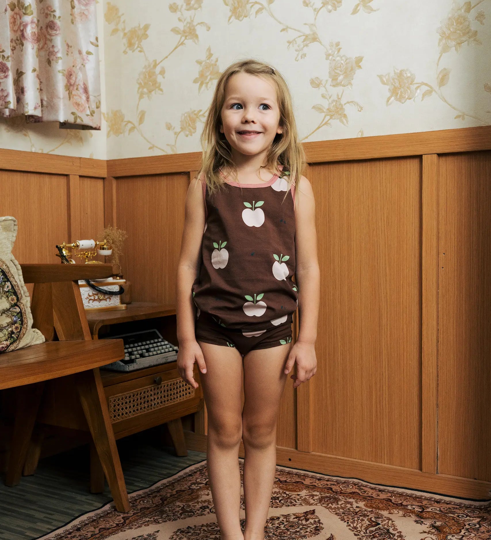 Girl wearing the Maxomorra's  GOTS organic cotton kids tank top in brown with a cute repeating pink apple print with matching trim with matching pants.