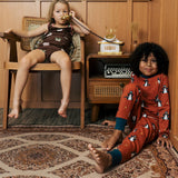 Two Children wearing Maxomorra organic cotton clothing. One is wearing a brown apple print vest and shorts the other is wearing a rust red blue dragon print long sleeved top with matching trousers.