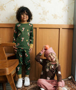 Child wearing Maxomora organic cotton green long-sleeve top with all over red fox print with matching pyjama trousers with a child sitting besides him wearing brown apple print top with pink trousers.