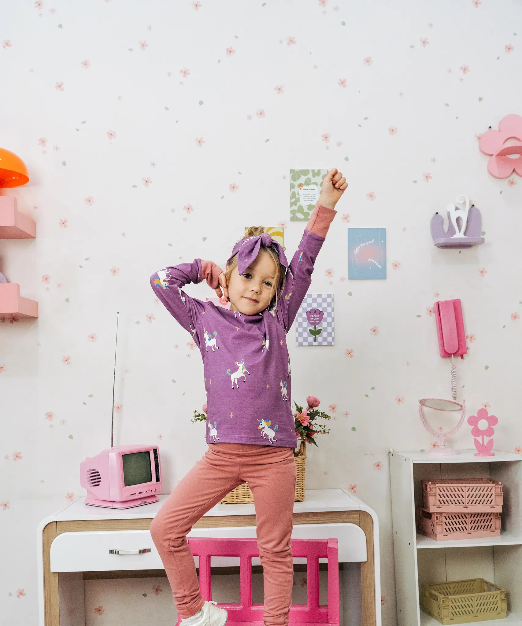 Child wearing the Maxomorra kids unicorns organic cotton long sleeve top with pink trousers. Purple top with  repeat unicorn print and light pink arm cuffs and binding on the neck. 
