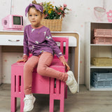 Child wearing the Maxomorra kids unicorns organic cotton long sleeve top with leggings. Purple top with  repeat unicorn print and light pink arm cuffs and binding on the neck. 