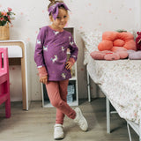 Child wearing the Maxomorra kids unicorns organic cotton long sleeve top with pink leggings. Purple top with  repeat unicorn print and light pink arm cuffs and binding on the neck. 