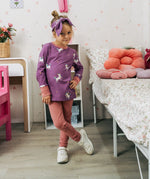 Child wearing the Maxomorra kids unicorns organic cotton long sleeve top with pink leggings. Purple top with  repeat unicorn print and light pink arm cuffs and binding on the neck. 