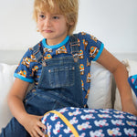 Young boy sat on a white sofa wearing the Maxomorra eco-friendly navy denim dungarees