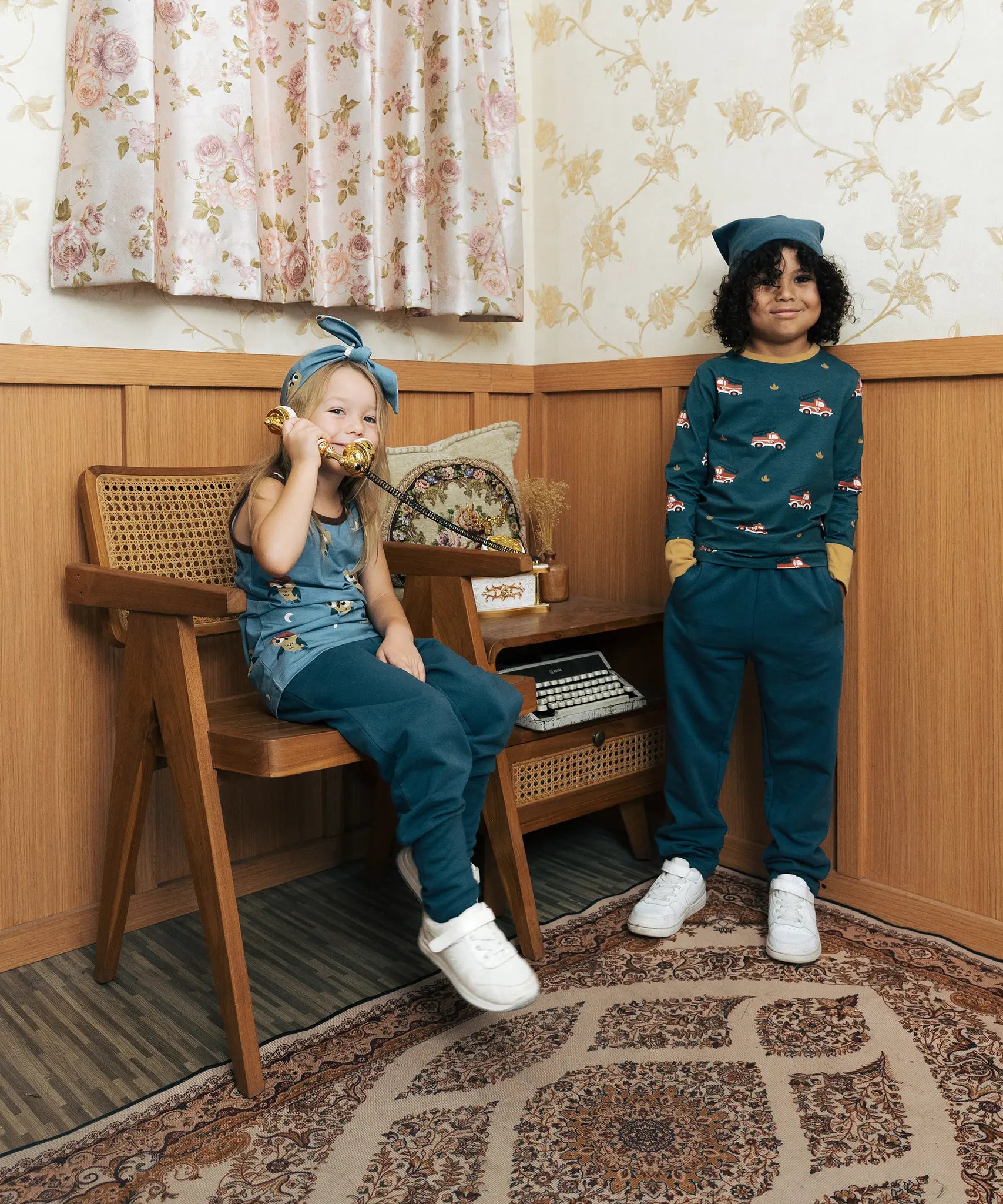 Two children wearing the Maxomorra kids baggy sweat pants in navy, features a drawstring cord around the waist and side pockets. One has a fire truck print top and one had an owl print vest top.