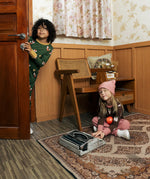 Child wearing Maxomora organic cotton green long-sleeve top. another child sitting on the floor wearing brown apple print top with pink trousers.