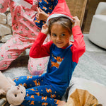 A child wearing the Maxomorra Reindeer Leggings with a coordinating reindeer print raglan top. The child is putting on a red Santa hat.