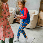 A child wearing the Maxomorra Reindeer Leggings with a coordinating reindeer print raglan top. The child is playing with Christmas streamer decorations. 