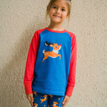 A child wearing a Maxomorra Reindeer Raglan Long Sleeve Top. The child is standing in front of a beige wall. 