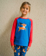 A child wearing a Maxomorra Reindeer Raglan Long Sleeve Top. The child is standing in front of a beige wall. 