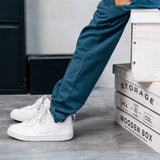 Close up of a child wearing the Maxomorra kids baggy sweat pants in navy, features a drawstring cord around the waist and side pockets with white sneakers.