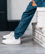 Close up of a child wearing the Maxomorra kids baggy sweat pants in navy, features a drawstring cord around the waist and side pockets with white sneakers.