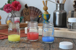 3 mercurius glass paint jar pots with lids taken off and some blue, red and yellow paint in them.