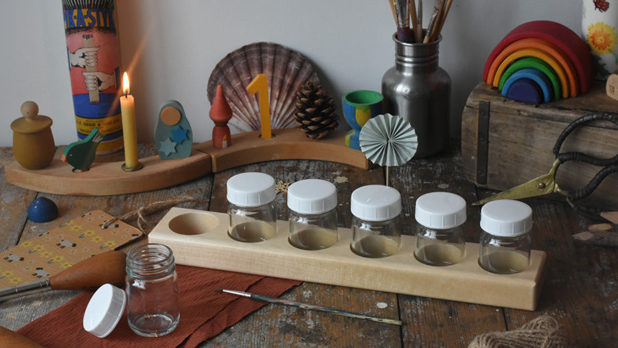Mercurius Waldorf art supplies; glass paint jars, wooden jar holder, and paintbrushes, set up in a seasonal scene in the Babipur art studio.