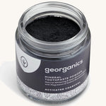  A opened jar of the charcoal Georganics toothpaste powder on a cream background