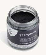 A opened jar of the charcoal Georganics toothpaste powder on a cream background